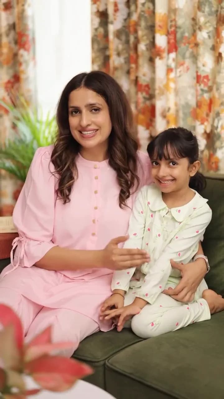 A woman and a young girl in pyjamas sit together on a green sofa and smile.