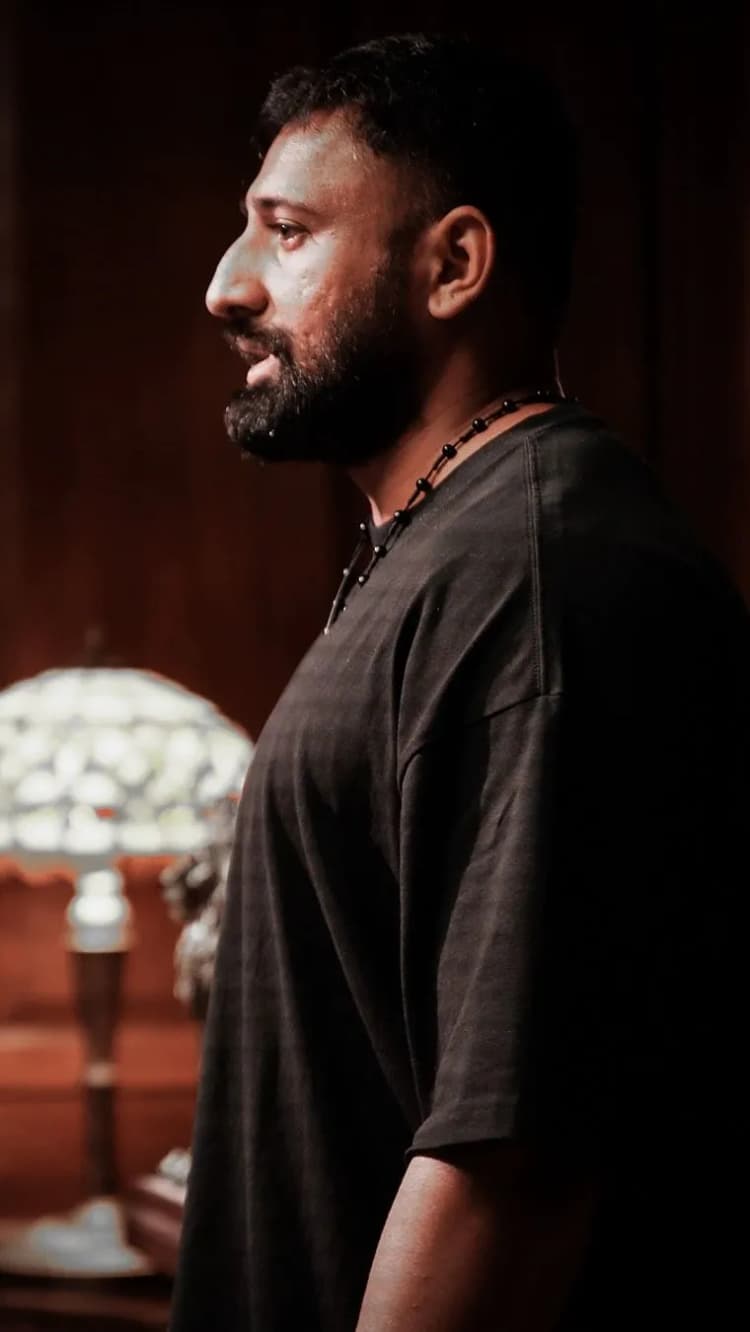 The creator in profile, bearded, in a black tee beside a lit lamp: the reel’s cover frame.