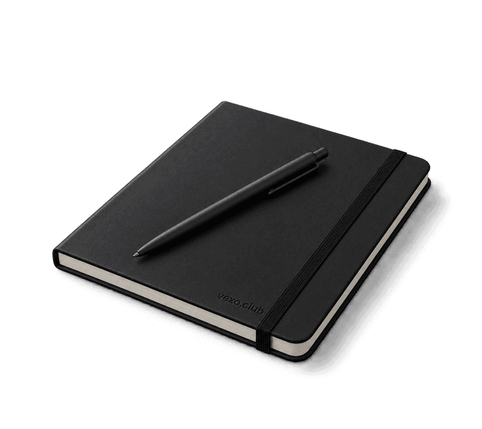 Black hardback notebook closed with its elastic band, a pen lying across it